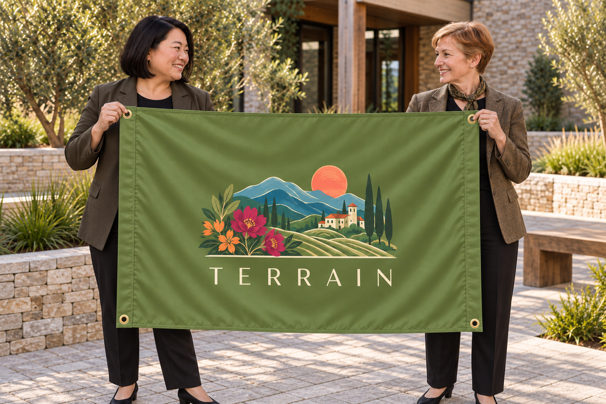 Illustrative campaign: adult business owners outside their workplace holding a customized olive green flag, 5 feet wide by 3 feet tall with vivid multicolor artwork and four corner grommets